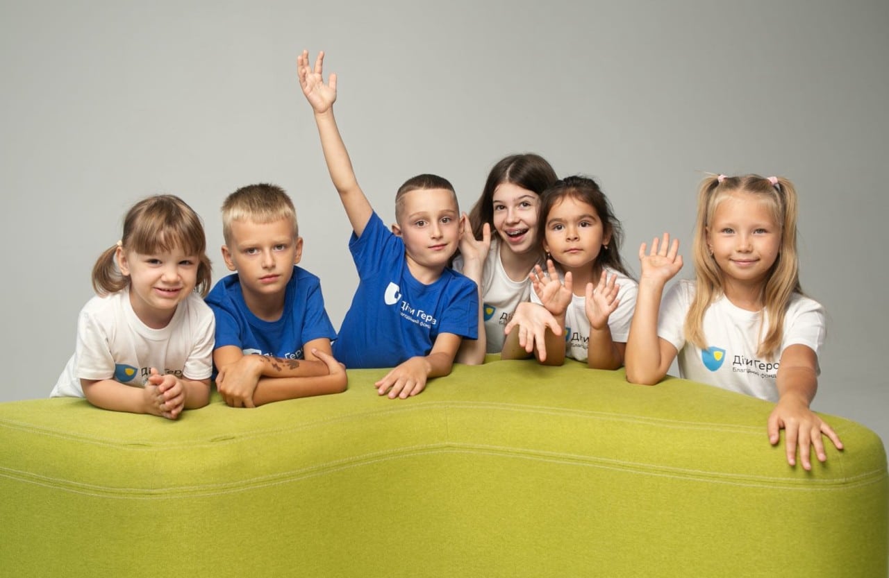 Children of Heroes. Six smiling children sitting around a lime green soft furnishing.